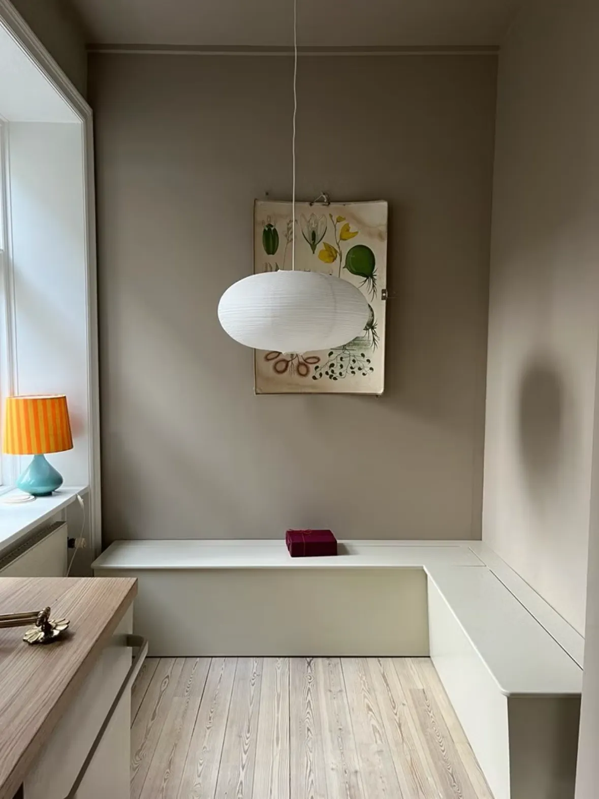 Hvid hjørneslagbænk under en papirlampe i en stue med varmgrå vægge