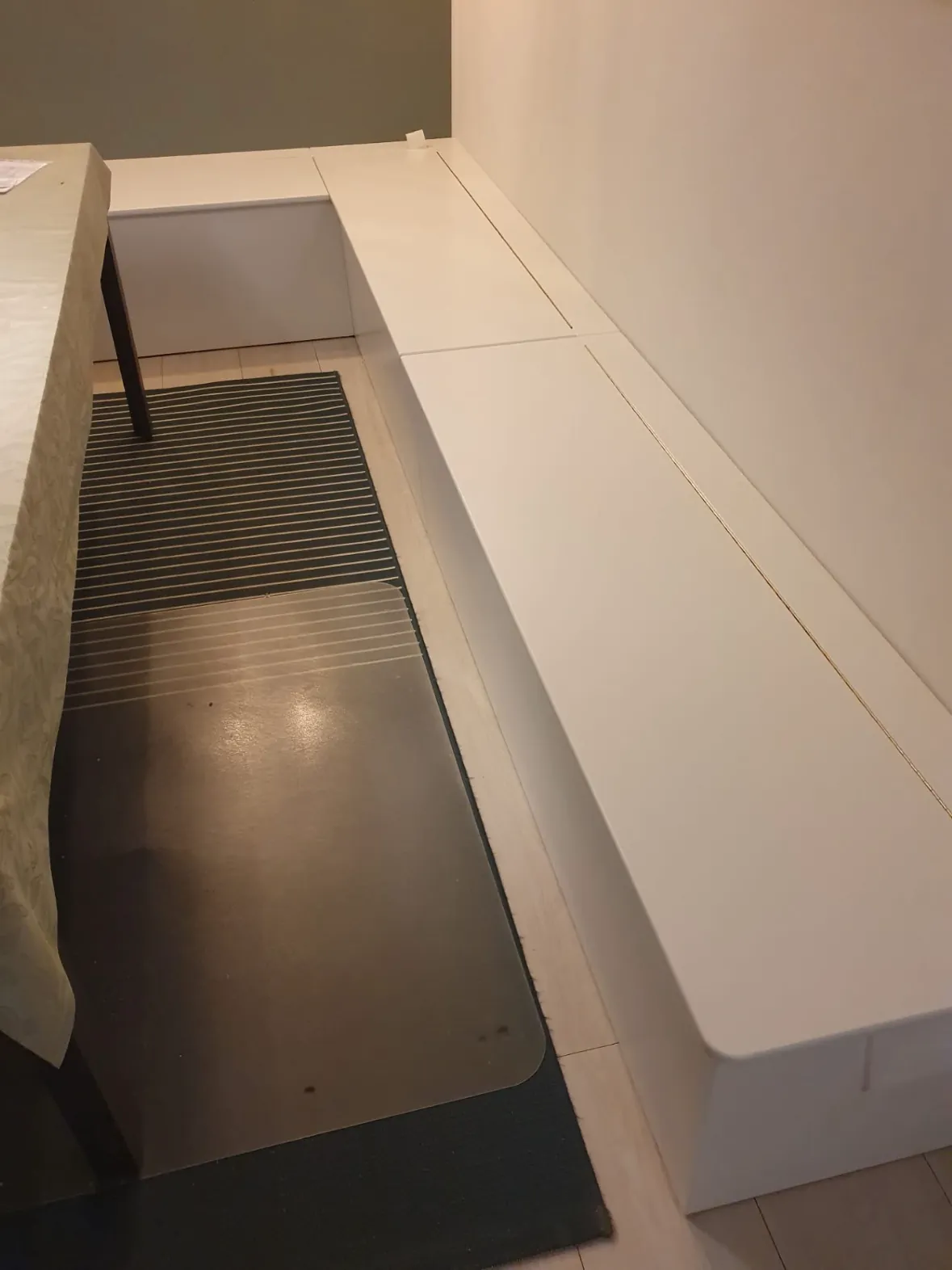 Lang hvid slagbænk med flere låg langs væggen ved et spisebord